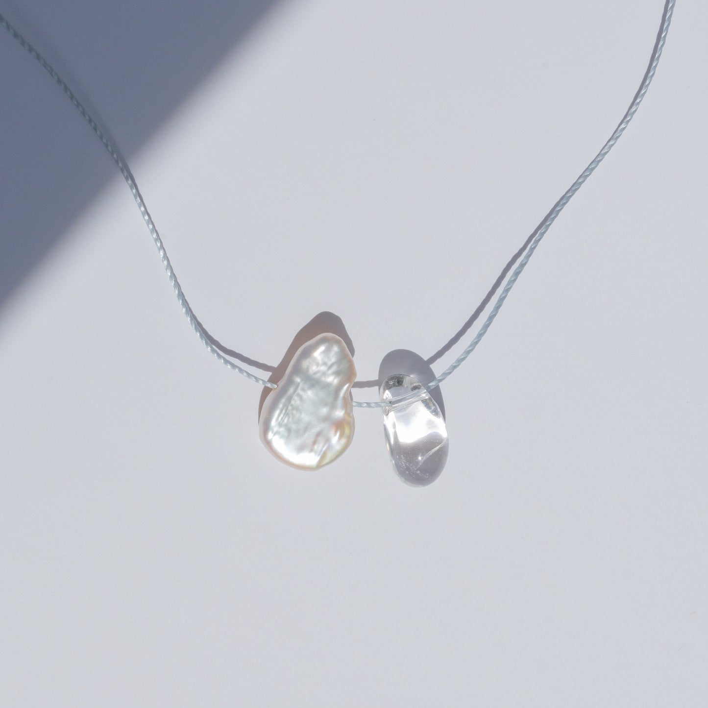 Delicate crystal quartz and baroque pearl necklace on light blue cord with sterling silver clasp.